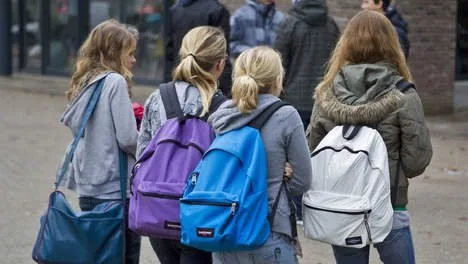 Brugklassers lopen samen met rugzakken op het schoolplein.
